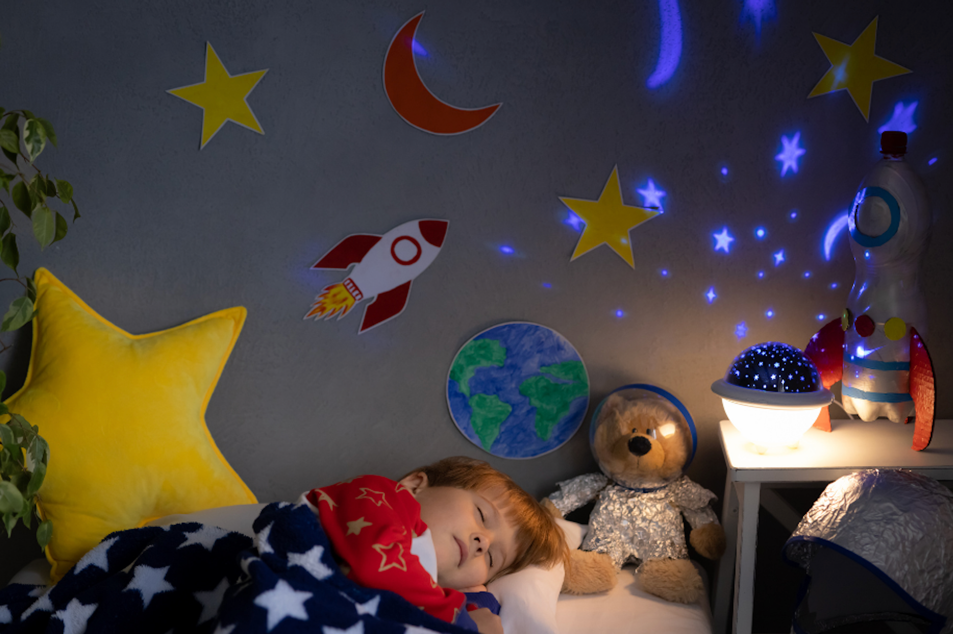 Ett barn som sover i ett barnrum dekorerat med galaxlampa, stjärnor och raketer